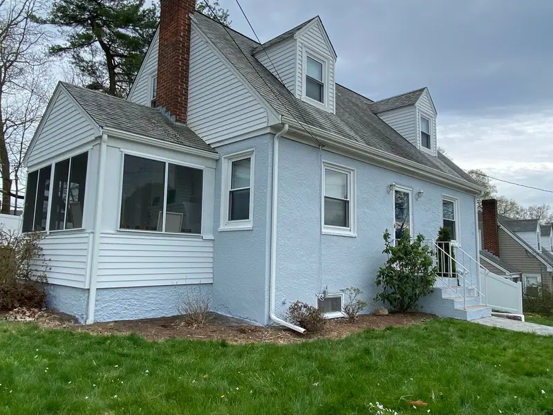White cape home with a sunroom and chimney after painting